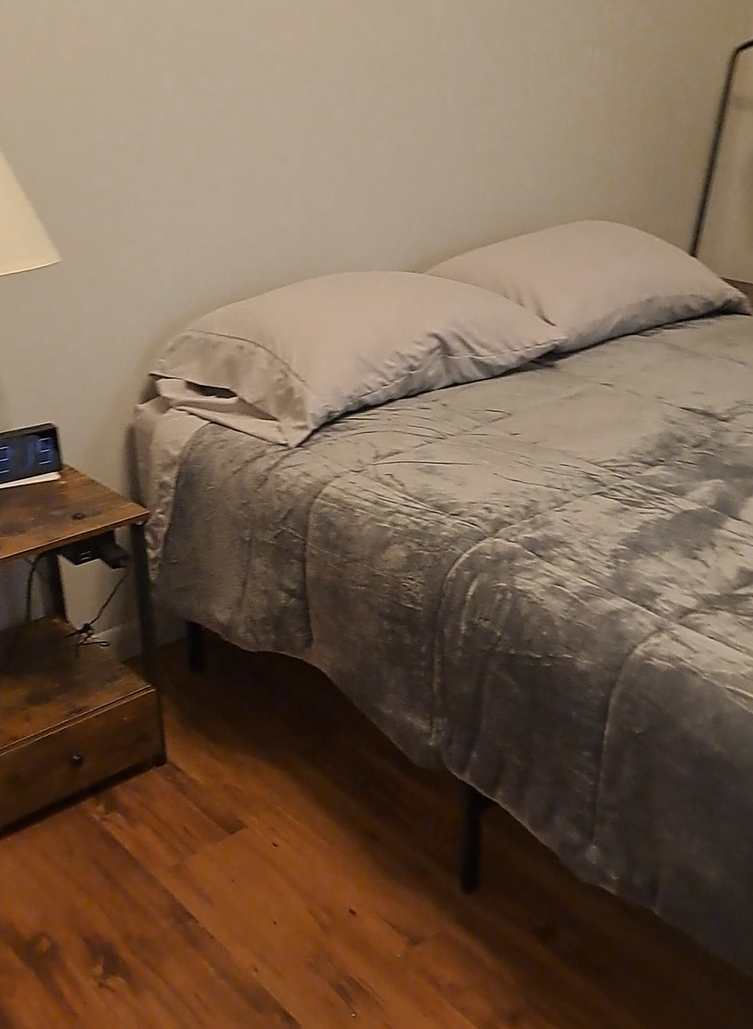 Bedroom with a made bed, side table, lamp, and wood floor.