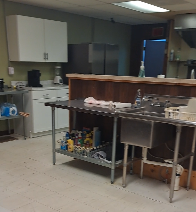 Professional-style kitchen with stainless work tables, large sinks, cabinets, and refrigerator.