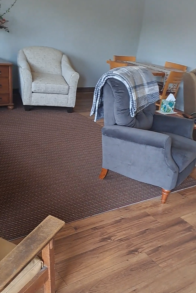 Living area with chairs, a small table, wood-look floors, and front entry nearby.